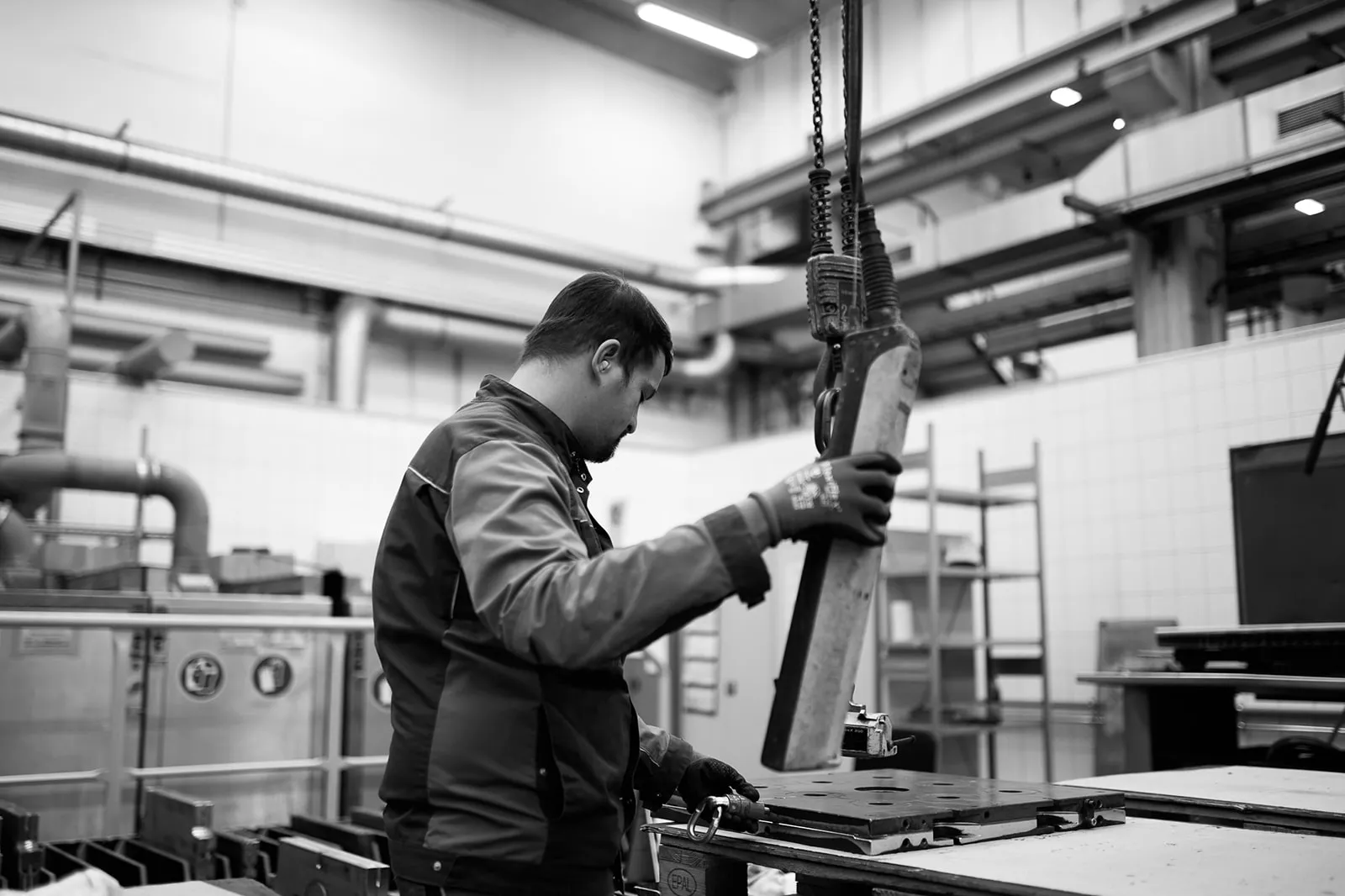 Mitarbeiter mit Arbeitshandschuhen führt einen Kranhaken an ein Werkzeug
